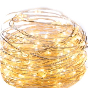 May include: A tightly coiled string of warm white LED fairy lights. The lights are on a thin, flexible silver wire, creating a soft, glowing effect. The lights are clustered together, creating a bright, festive appearance, perfect for decorating.