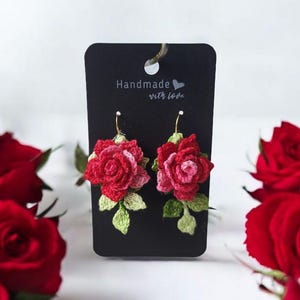 May include: Crocheted rose earrings with green leaves, displayed on a black card with the text "Handmade with love".
