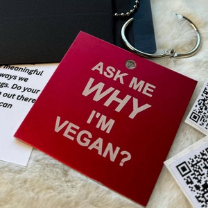 May include: A red keychain with the text "Ask Me Why I'm Vegan?" and two black and white QR codes. The keychain is attached to a silver chain.