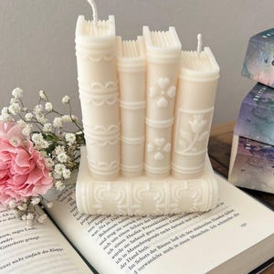 May include: A set of three white candle books with decorative details. The candles are stacked on top of each other and have a vintage book look.