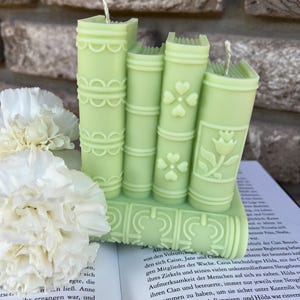 May include: A set of four green book-shaped candles with white wicks. The candles are stacked on top of each other and have a floral design.