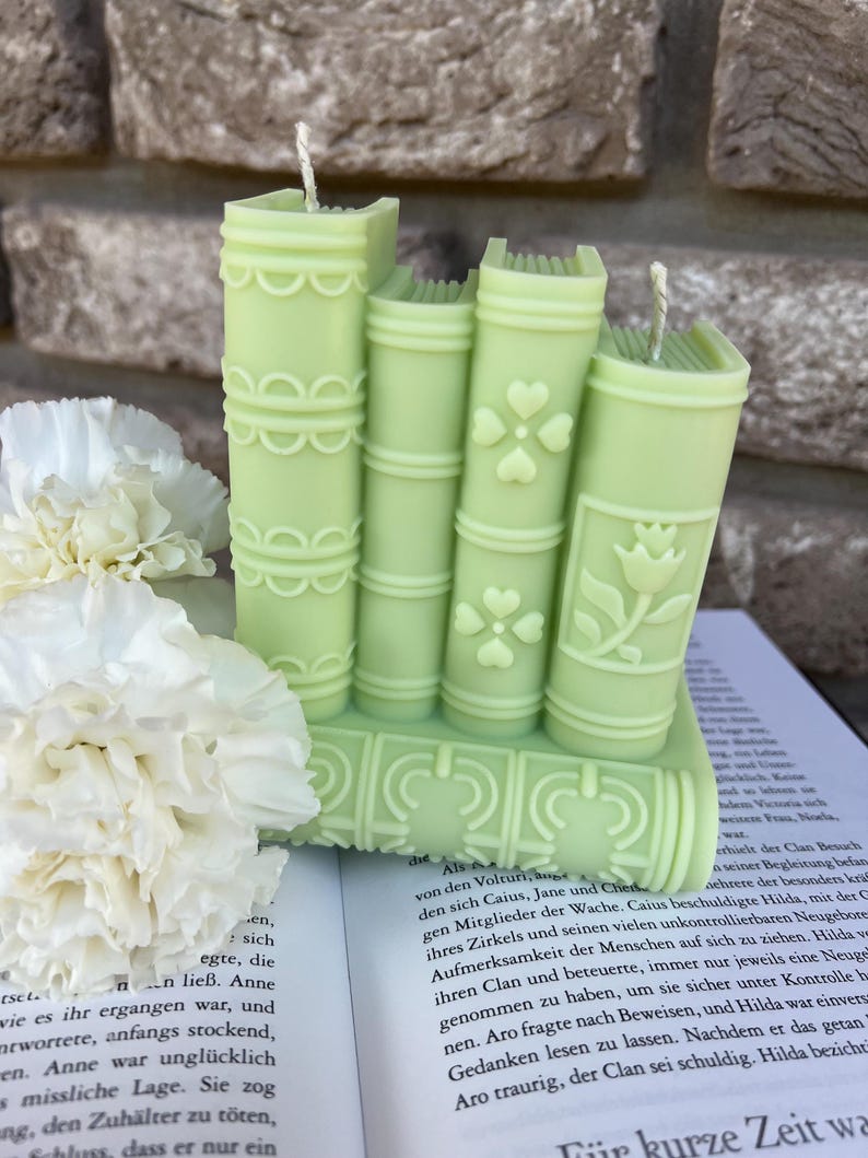 May include: A set of four green book-shaped candles with white wicks. The candles are stacked on top of each other and have a floral design.