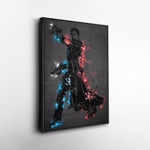 May include: A framed art print featuring a stylized silhouette of a figure holding two guns, with red and blue accents. The artwork has a dark background with paint splatter effects, creating a dynamic and action-oriented aesthetic.
