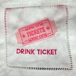 Puede incluir: Servilleta de c&oacute;ctel de lino blanco con un dise&ntilde;o de boleto bordado en rosa. El boleto dice "TICKETS" y "Admit One". Debajo del boleto, las palabras "DRINK TICKET" est&aacute;n bordadas en rosa.