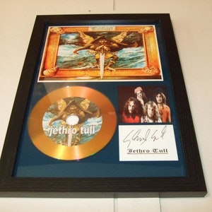 Könnte beinhalten: Gerahmte Jethro Tull-Erinnerungsstücke, darunter eine goldene CD, ein Bandfoto und eine signierte Autogrammkarte. Das Kunstwerk zeigt eine Kriegerfigur mit einem Schwert. Der Rahmen ist schwarz, mit blauem Passepartout.