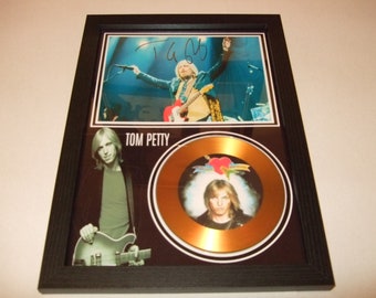 May include: Framed Tom Petty memorabilia featuring a signed photograph and a gold record. The photograph shows Petty performing on stage. The gold record has a portrait of Petty and a heart logo. The frame is black.