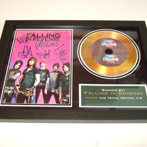 Op de afbeelding: Een ingelijste gouden plaat met een zwarte lijst en een gouden schijf. De schijf heeft de naam van de band "Falling in Reverse" erop gedrukt. De lijst bevat ook een gesigneerde foto van de band met de handtekeningen van de bandleden. De tekst "Signed by: Falling in Reverse" en "Origin: Las Vegas, Nevada, U.S." is op de lijst gedrukt.