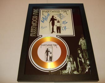 May include: A gold record framed in a black frame. The record features a picture of Fleetwood Mac and the text "Fleetwood Mac". The frame also includes a signed album cover with the signatures of the band members.