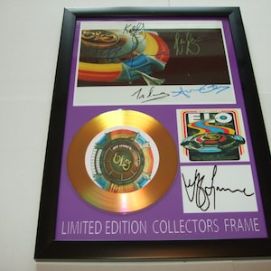 Puede incluir: Un disco de oro en un marco morado con una foto de la banda Electric Light Orchestra (ELO) y sus firmas. El disco es un marco de coleccionista de edición limitada.