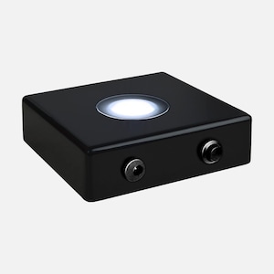 May include: A black square display base with a white LED light in the center. The base has two ports on the side for power and connection.