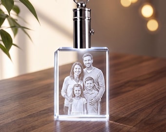 May include: A rectangular clear glass block keychain featuring a laser-etched three-dimensional portrait of a family of four. The crystal block is attached to a polished silver-colored metal cylindrical cap with a circular ring for attachment.
