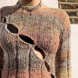 May include: A brown, orange, and grey knit sweater with a distressed look. The sweater has several large holes in the front and sleeves.