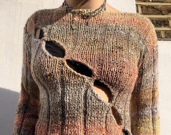 May include: A brown, orange, and grey knit sweater with a distressed look. The sweater has several large holes in the front and sleeves.