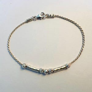 May include: A silver bracelet with a rope chain and five small, textured silver beads. The beads are connected by three silver bars.