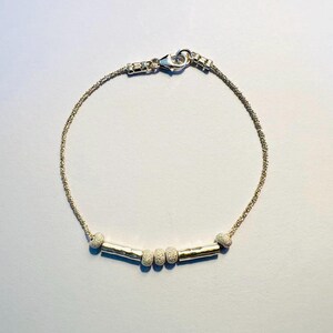 May include: A silver chain bracelet with a row of small, textured silver beads.