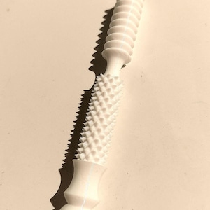 May include: A white massage tool with a textured design. The tool has a cylindrical shape with ridges and a section covered in small, cone-shaped bumps. The handle has a rounded base and a smooth, curved design.