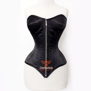 May include: A black corset featuring a sweetheart neckline, structured cups, and a vertical silver-toned metal zipper closure running down the center front. The garment displays a smooth, satin-like finish with visible vertical seams and a logo reading ClothoHub.
