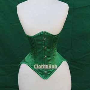 Può includere: Un corsetto in satin verde con chiusura a busc e occhielli in metallo. Il corsetto è su un manichino bianco. Il testo "ClothoHub The Original Corset Manufacturing Company" è stampato sul davanti del corsetto.