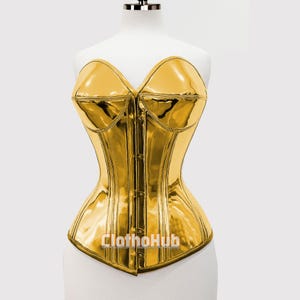 May include: A shiny gold corset with a sweetheart neckline and a structured silhouette. The corset features a series of small buttons down the front and is displayed on a white mannequin. The text "Clothohub" is visible at the bottom.