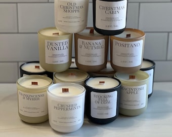 Puede incluir: Colección de velas perfumadas en frascos de vidrio con mechas de madera. Las etiquetas muestran varios aromas como "Old Christmas Shoppe", "Christmas Cabin" y "Crushed Peppermints". Cada vela es de 70g.
