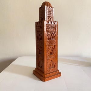 Peut inclure: Une tour décorative marron avec des détails sculptés complexes. La tour présente une base carrée, un corps rectangulaire avec des fenêtres cintrées et un sommet en forme de dôme. La conception comprend des briques et des motifs géométriques.