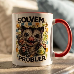 Może przedstawiać: Biały ceramiczny kubek z czerwonym wnętrzem i uchwytem. Kubek przedstawia kreskówkowego oposa trzymającego klucz i kolbę z zielonym płynem. Tekst na kubku brzmi "SOLVEM PROBLER" ze żarówką i znakiem zapytania.