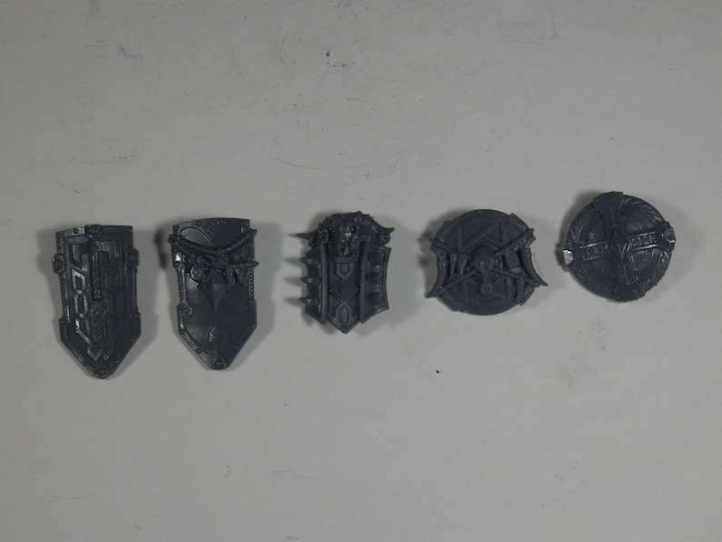 May include: Five gray plastic shields with different designs. The shields are all about 2 inches in diameter.