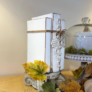 May include: White painted decorative bookends with a distressed finish and a decorative scroll design. The bookends are tied together with twine and are sitting on a table with autumn leaves.