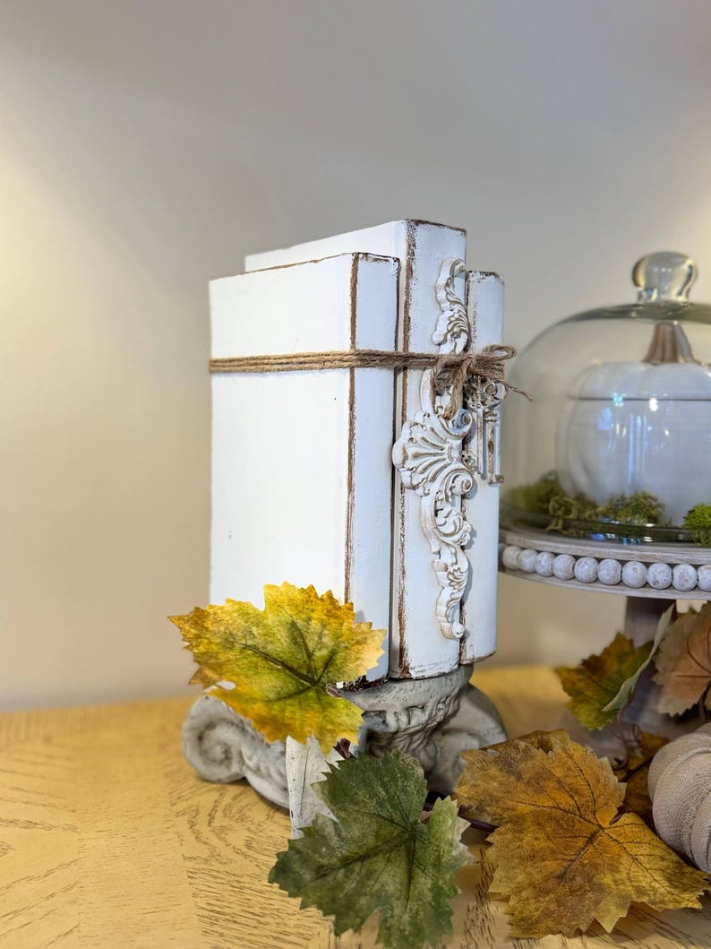 May include: White painted decorative bookends with a distressed finish and a decorative scroll design. The bookends are tied together with twine and are sitting on a table with autumn leaves.
