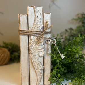 May include: A stack of three white painted wooden blocks with a decorative carved design on the centre block. The blocks are tied together with twine and decorated with a silver key.