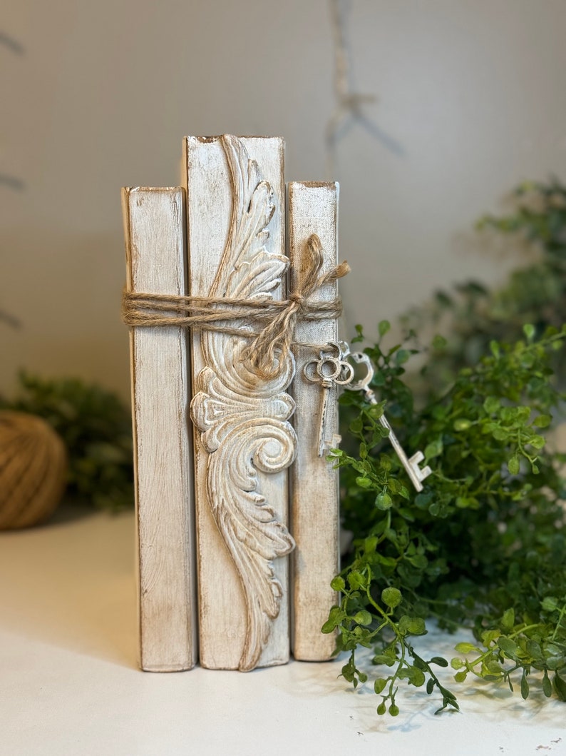 May include: A stack of three white painted wooden blocks with a decorative carved design on the centre block. The blocks are tied together with twine and decorated with a silver key.