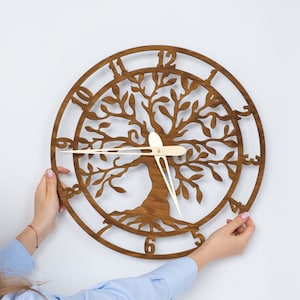 May include: A wooden wall clock featuring a tree of life design. The clock has a brown finish with a circular frame and Roman numerals. The clock hands are a light beige color.