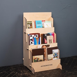 Puede incluir: Una estantería de madera con múltiples estantes, que muestra varios libros. La estantería es de madera de color claro y tiene un diseño escalonado. El texto "ANTONENKOSTORE" está impreso en la parte delantera de la estantería.