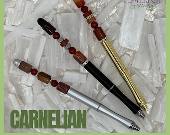 May include: Three pens with carnelian gemstone accents. One pen is gold, one is black, and one is silver. The pens have a decorative design with red and brown beads. The word "CARNELIAN" is displayed in green text.