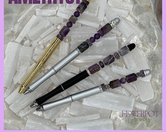 May include: Four pens featuring amethyst bead accents on the upper barrels. The pens have gold, silver, and black finishes with metallic hardware. The word AMETHYST is printed at the top, and Flowerpot Greenery is printed at the bottom right.