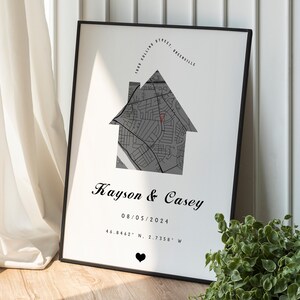 May include: A black and white framed print with a house-shaped map of a neighborhood. The text "Kayson & Casey" is below the map, along with the date "08/05/2024" and coordinates "46.8462° N, 2.7358° W".