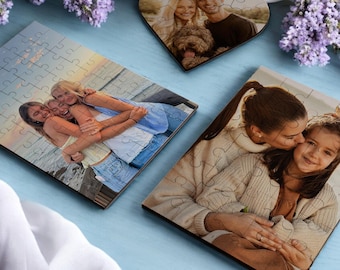 May include: Three wooden jigsaw puzzles with different photos. The first puzzle shows three women hugging on a beach at sunset. The second puzzle shows a woman kissing a young girl on the cheek. The third puzzle shows a couple with a dog.