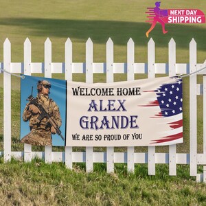 Op de afbeelding: Welkom thuis banner met een foto van een soldaat in camouflage die een geweer vasthoudt. De banner zegt "Welkom thuis Alex Grande We zijn zo trots op je" en heeft een Amerikaanse vlag op de achtergrond.