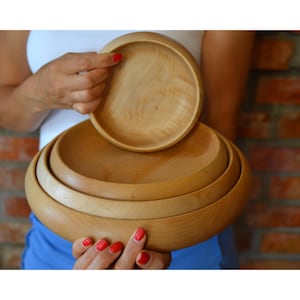 May include: A set of three wooden bowls, nested together. The bowls are made of light-coloured wood and have a smooth, natural finish.