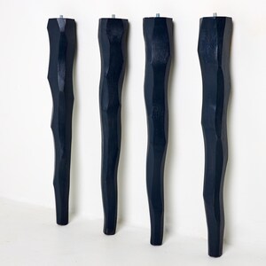 May include: A set of four tall, dark navy blue furniture legs with a faceted, irregular, and wavy vertical silhouette. Each leg features a metallic threaded bolt protruding from the top end for attachment purposes, showcasing a matte finish.