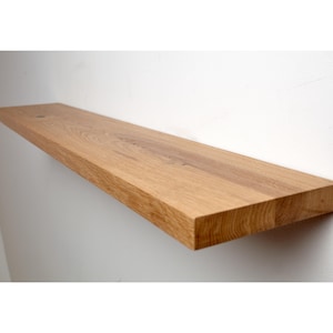 Puede incluir: Estante flotante rectangular de madera clara, montado en una pared blanca. La madera muestra vetas visibles. El estante mide aproximadamente 91 cm de largo y 20 cm de ancho.