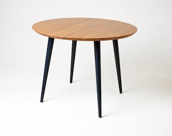 Könnte beinhalten: Ein runder Holztisch mit einer hellbraunen Tischplatte und vier dunkelblauen Beinen. Der Tisch steht vor einem weißen Hintergrund und zeigt sein schlichtes, modernes Design. Die Tischplatte hat einen Durchmesser von ca. 76 cm.