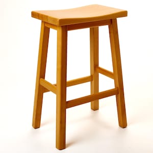Könnte beinhalten: Ein hellbrauner Barhocker aus Holz mit einer geschwungenen Sitzfläche und vier stabilen Beinen. Der Hocker ist aus massivem Holz gefertigt und hat ein schlichtes, klassisches Design. Der Sitz ist ca. 38 cm breit.
