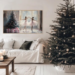Puede incluir: Una pintura enmarcada de dos bailarinas en tut&uacute;s blancos bailando frente a un &aacute;rbol de Navidad con regalos debajo. La pintura est&aacute; colgada en una pared blanca sobre un sof&aacute; blanco con un coj&iacute;n verde.