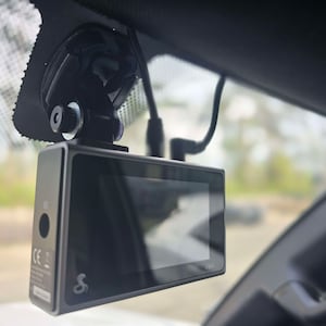 May include: A black dash cam with a screen displaying "4K" mounted on a windshield using a suction cup mount.