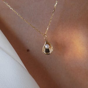 May include: A gold chain necklace with a delicate gold seashell pendant featuring a small white pearl.