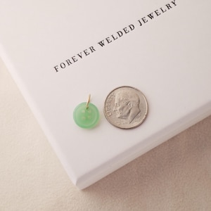May include: A light green button pendant with a gold bail next to a dime on a white surface. The pendant is round with four holes and a slightly raised design. The text "FOREVER WELDED JEWELRY" is printed on the white surface.