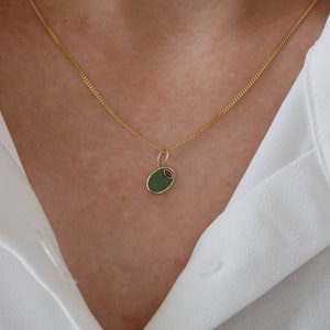 Puede incluir: Un collar de cadena dorada con un colgante ovalado verde con un detalle rosa.
