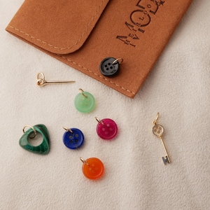May include: A collection of colorful charms and pendants, including a green heart, a gold key, and button-shaped charms in various colors. A small brown pouch with gold lettering is also present.