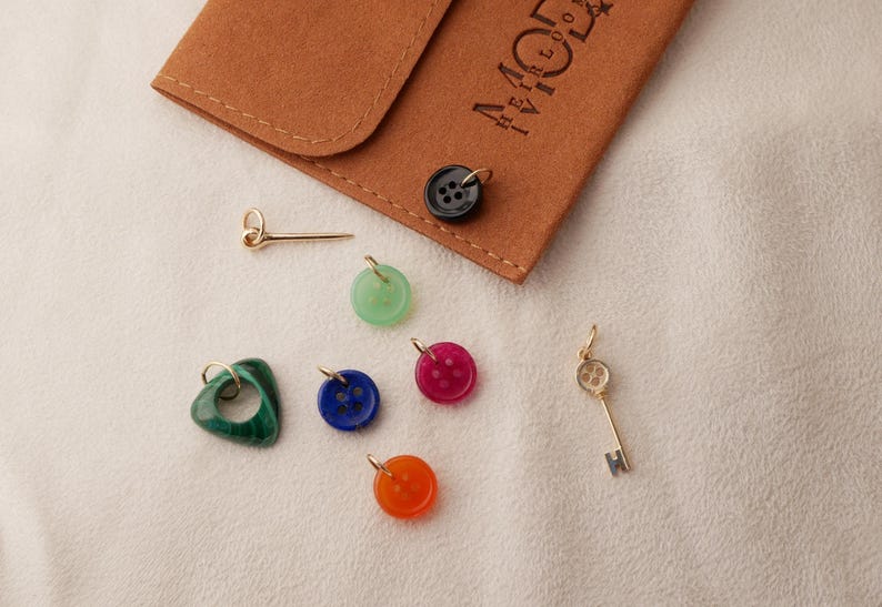 May include: A collection of colorful charms and pendants, including a green heart, a gold key, and button-shaped charms in various colors. A small brown pouch with gold lettering is also present.